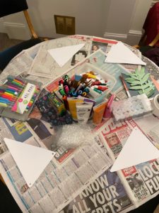 Table covered in newspaper with craft materials, including felt tip pens and crayons