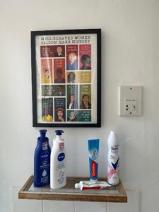 Toiletries on a shelf in front of poster showing images of powerful women