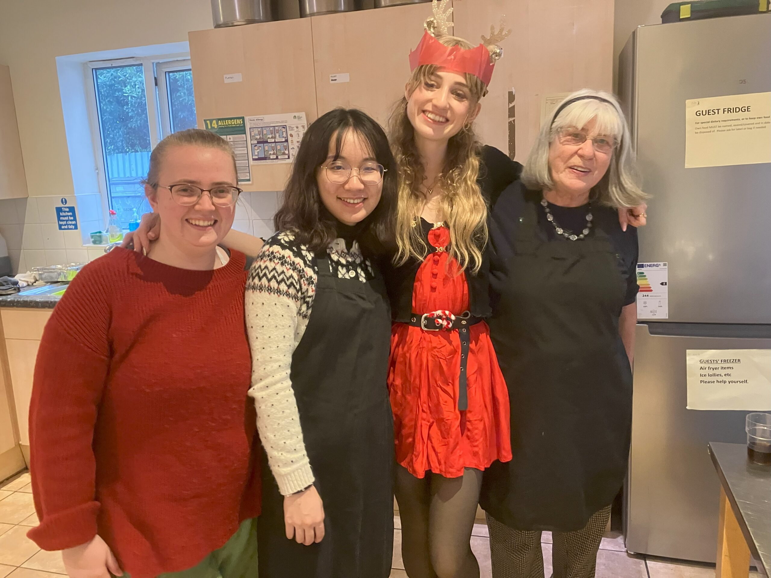 Four female volunteers with arms around each other and smiling at the camera. They are standing in a large kitchen
