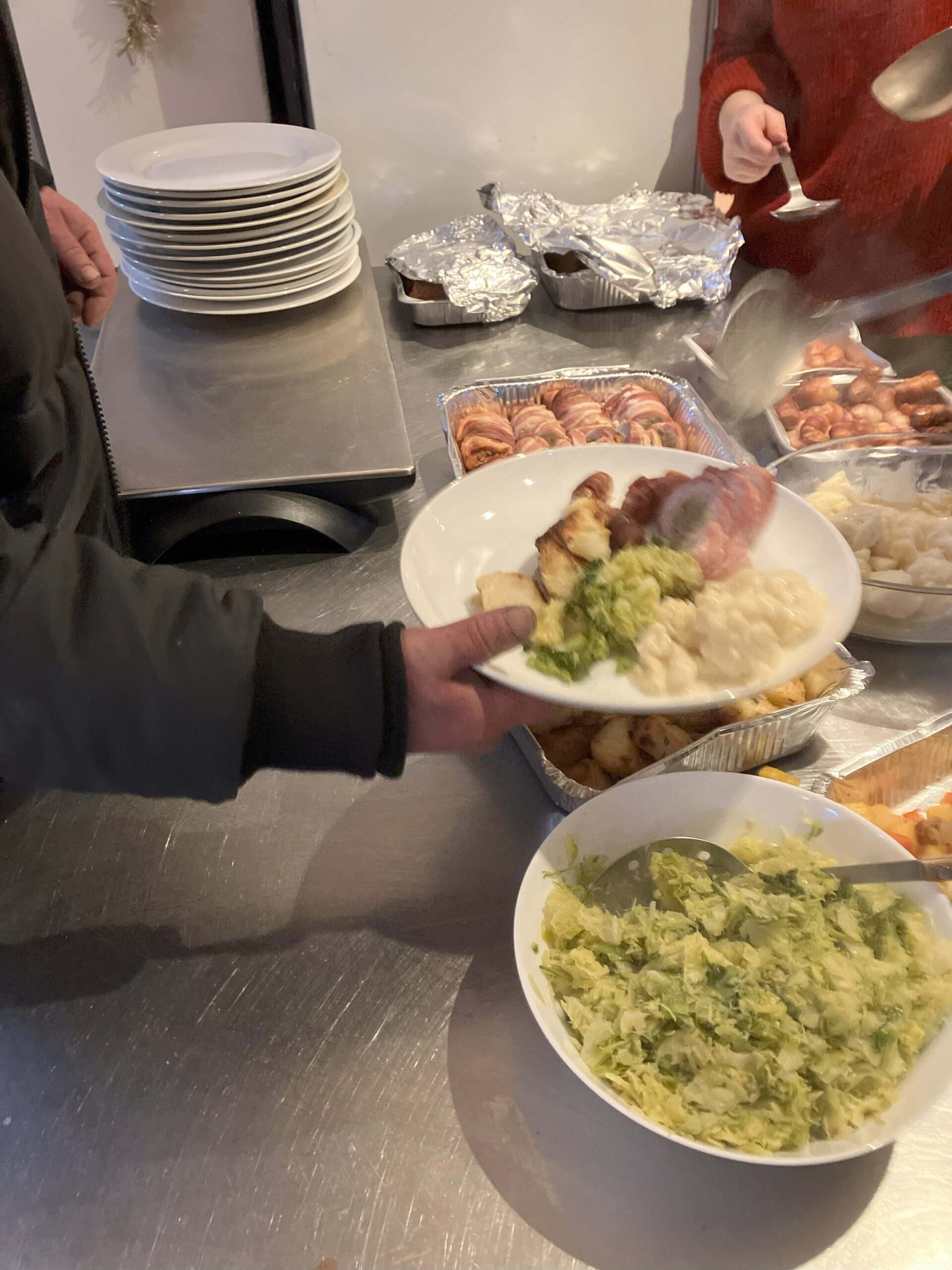 Person being served Christmas dinner atCrossways. There is a plate in the foreground with several serving dished full of different food stuffs behind the plate