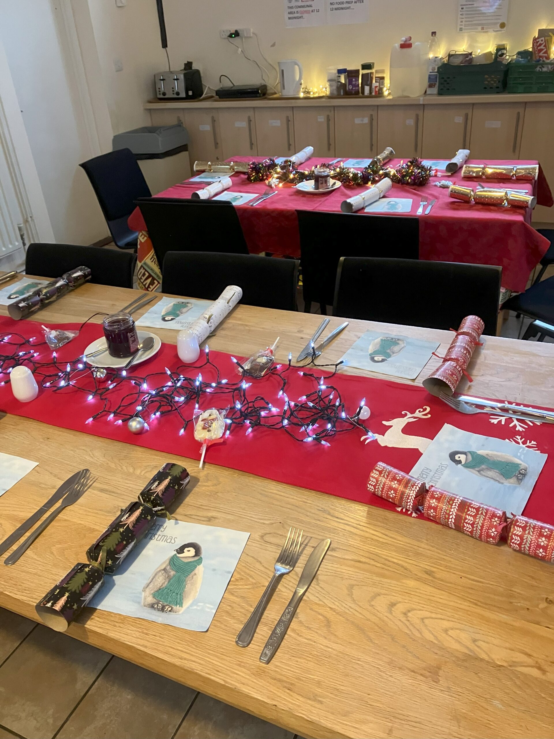 Two long dining tables decorated for Christmas dinner with lights and crackers