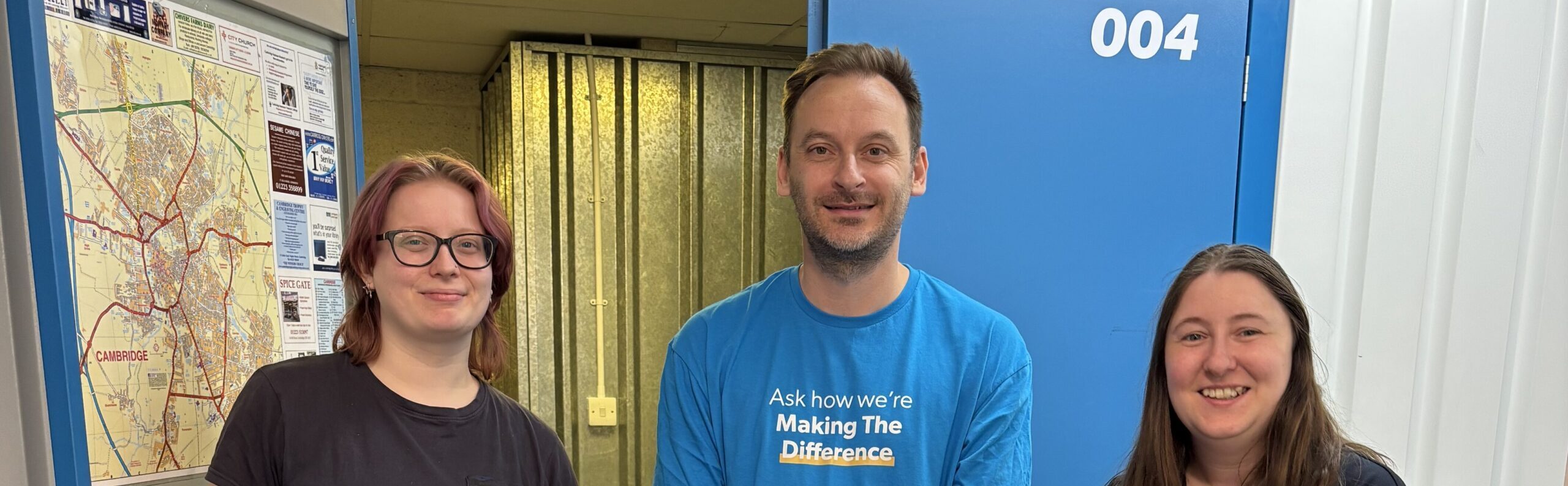 Rory from It Takes A City, Simon from Cambridge Building Society and Solitaire from Pickfords stand behind a trolley with three suitcases on it