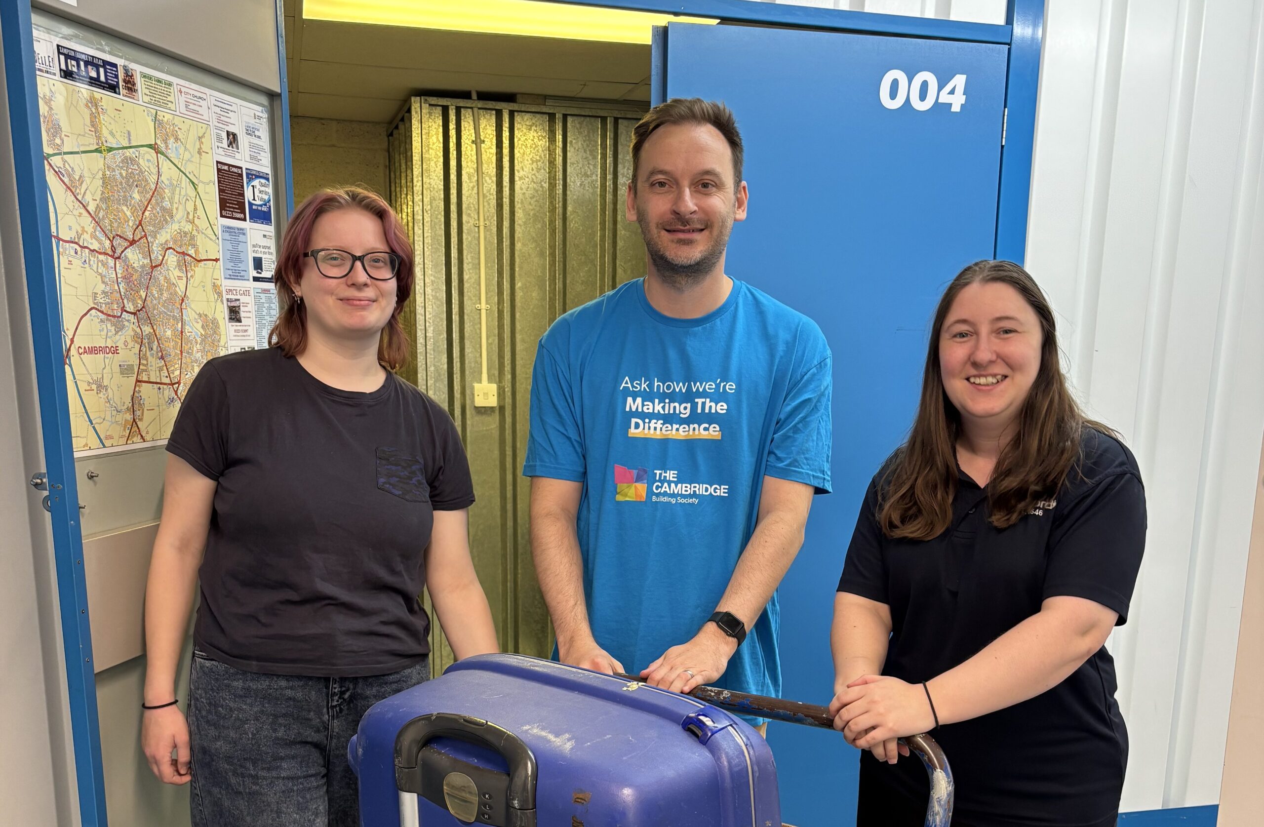Storage_Volunteer1 Rory from It Takes A City, Simon from Cambridge Building Society and Solitaire from Pickfords stand behind a trolley with three suitcases on it
