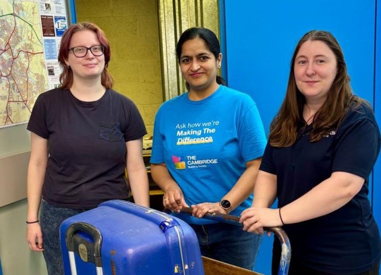 Rory from It Takes A City, Mukta from Cambridge Building Society and Solitaire from Pickfords stand behind a trolley with three suitcases on it