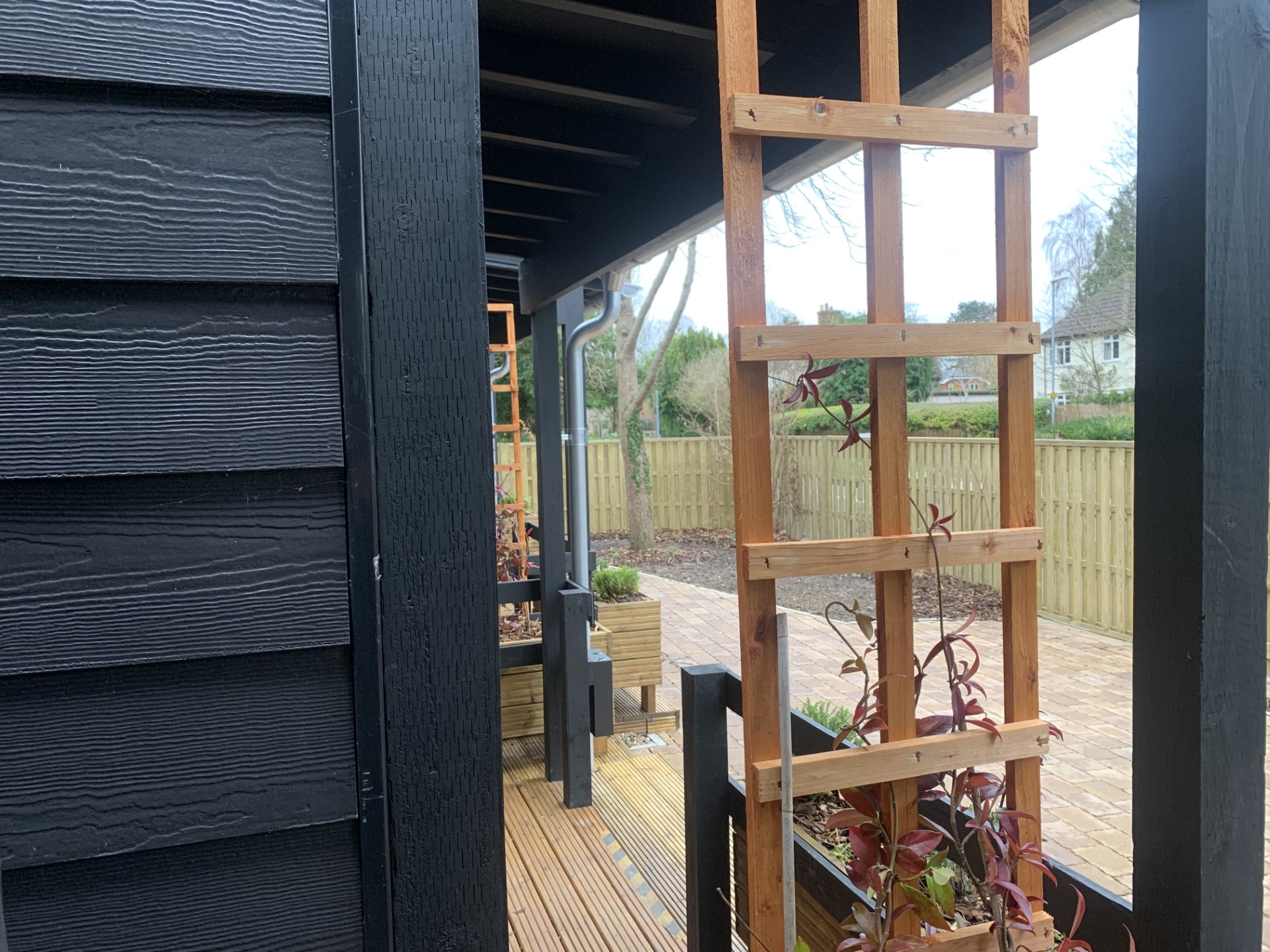 Looking through some trellis from the side angle of a modular home. In the background can be seen some low garden fencing with detached houses beyond