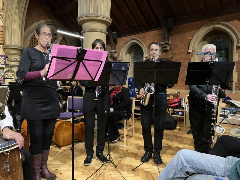 Four woodwind musicians stand behind music stands in a church setting