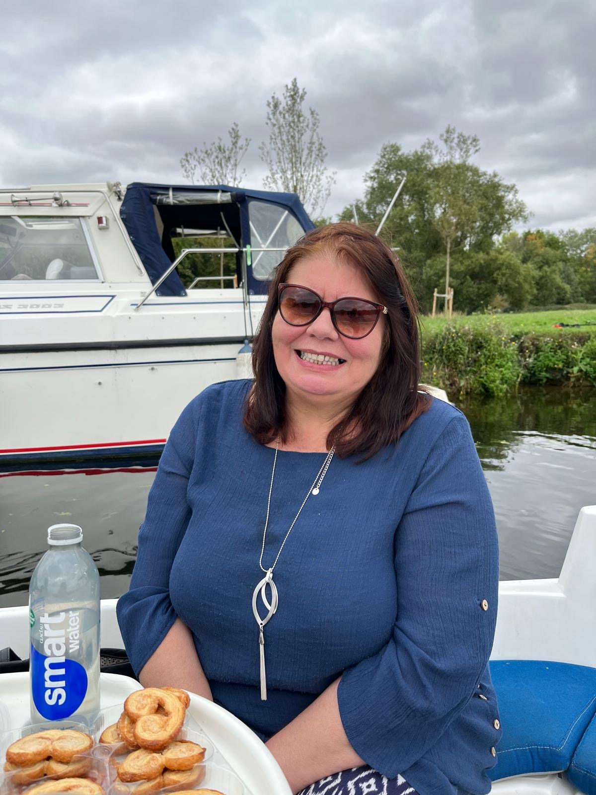 A photo of Lesley Crocker, supporter of ITAC, sitting on a boat on a river. You can see the far bank with another boat moored