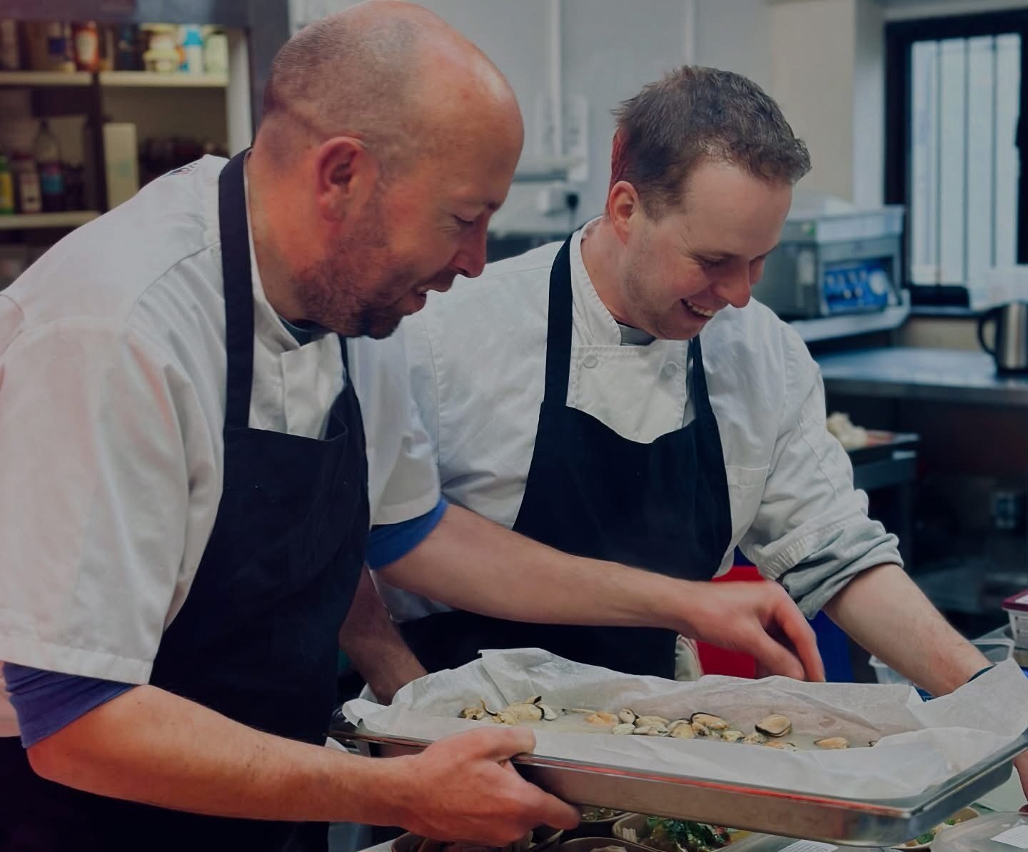 Two chefs in kitchen preparing meals in recyclable containers.