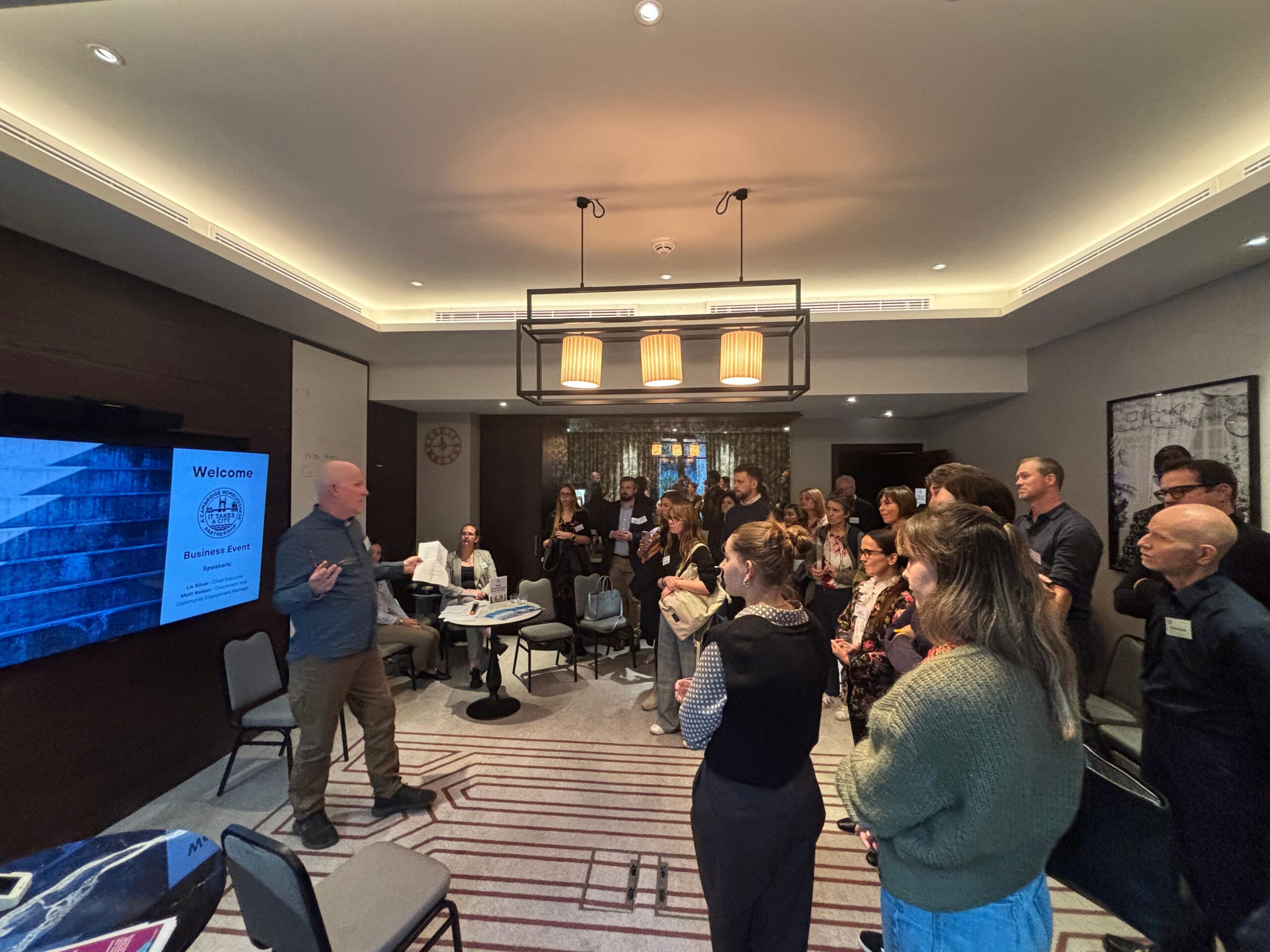Matt delivering a speech to an audience of potential sponsors in front of a display screen saying "welcome to our business event"