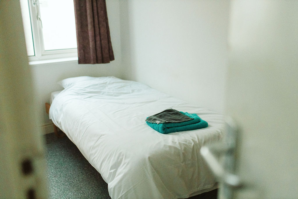 Looking through an open door at a bed with towel and flannel on the quilt, waiting to a resident to arrive