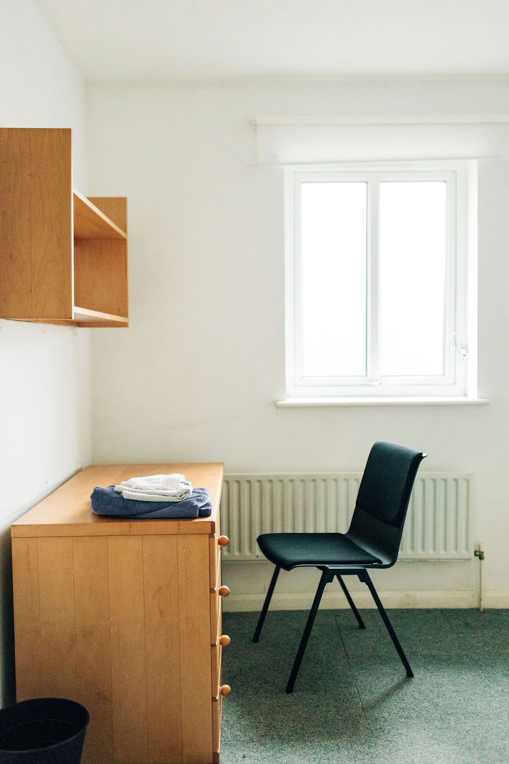 A small writing desk and chair with bookshelf above and window at the back in a room in Crossways