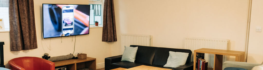 View of three sofas, coffee table and large, wall mounted TV in the Crossways lounge