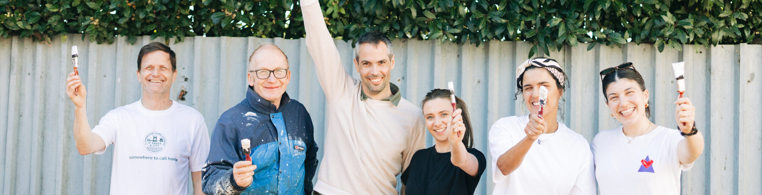 CorporateVolunteers2026-ebp2026-24 Volunteers from Cogentia stand with Barry and hold up paintbrushes in front of flower beds