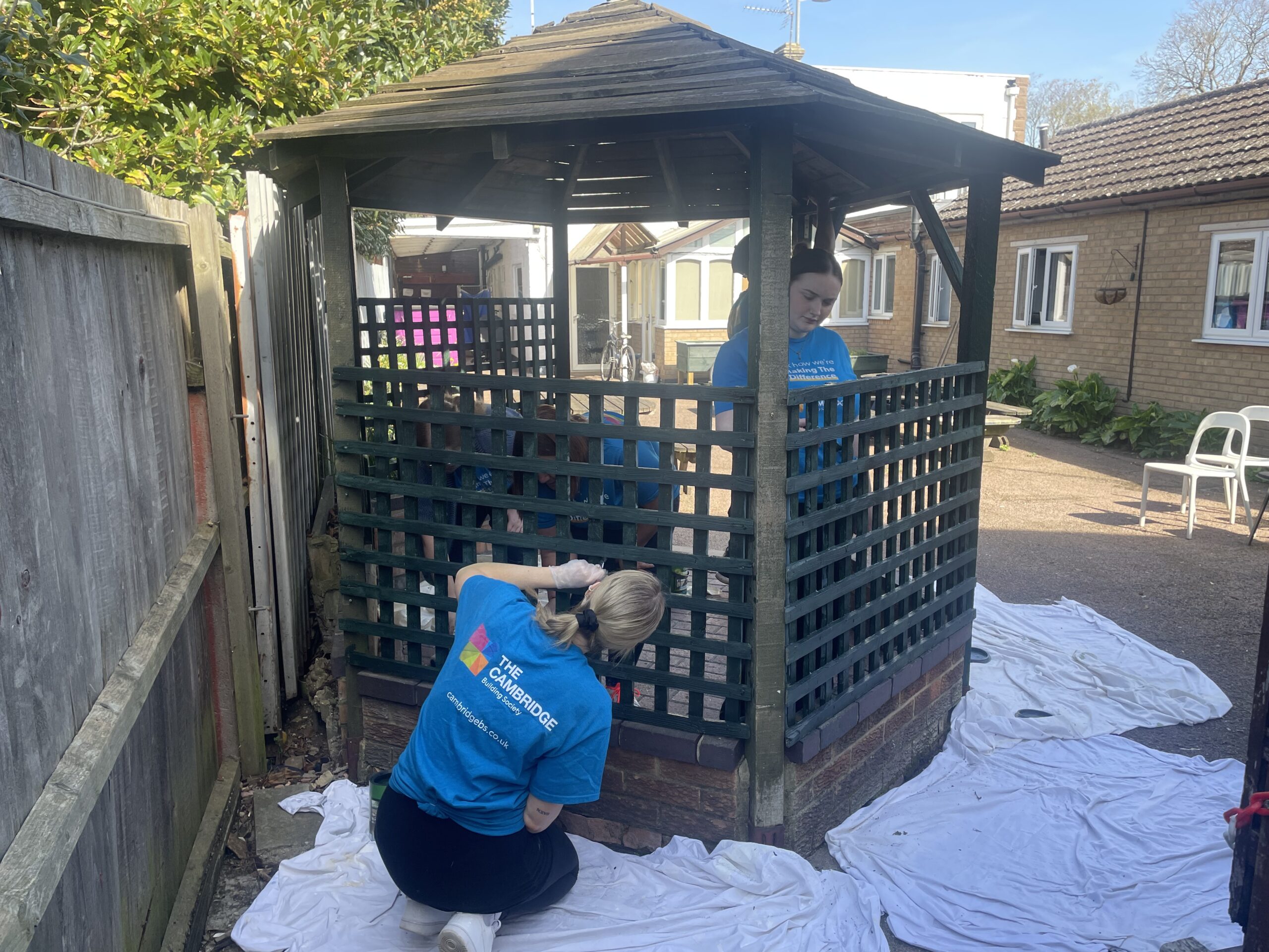 Volunteers wearing CBS t shirts paint the pergola in Crossways garden