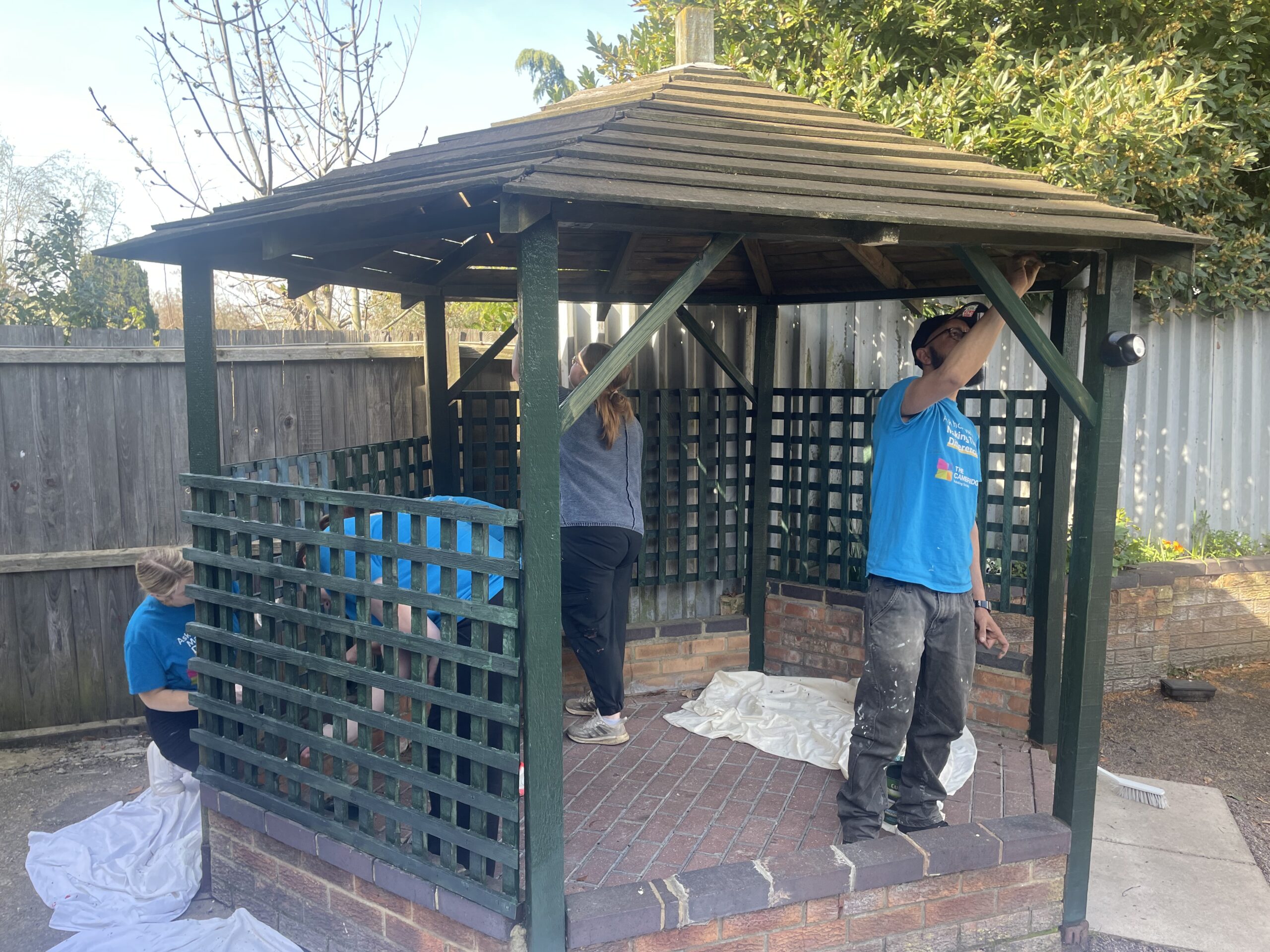 Volunteers wearing CBS t shirts paint the pergola in Crossways garden