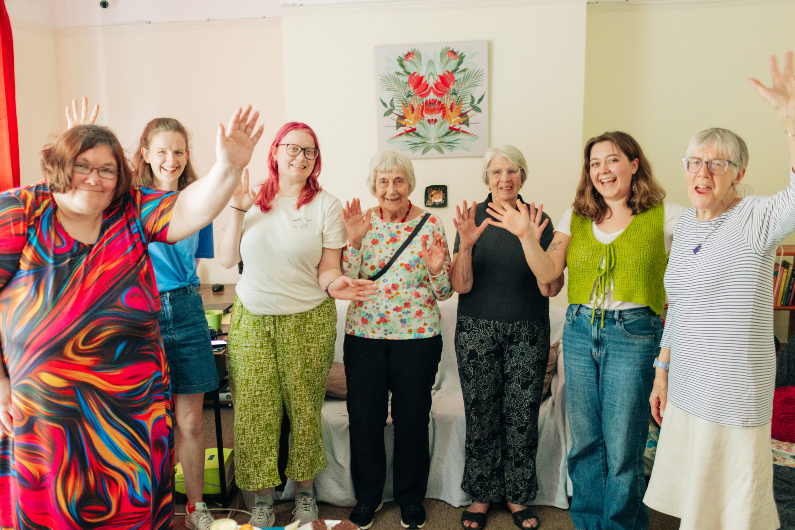 A group of seven women are cheering and waving in celebration in front of a picture of stylised flowers in the Haven lounge
