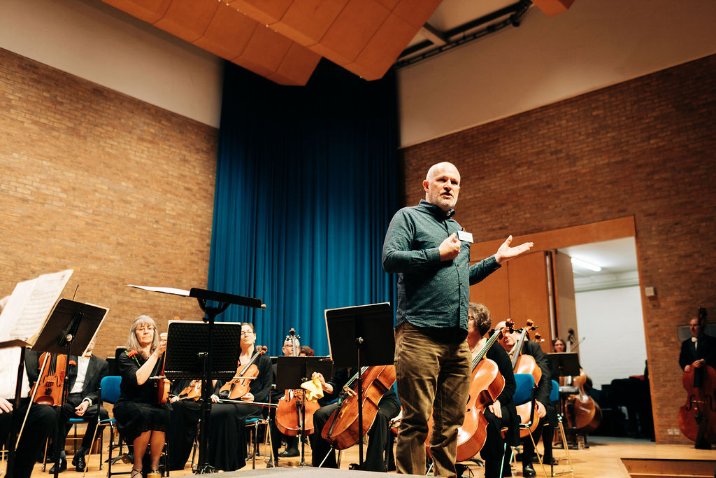 Matt speaks to audience from the stage of a charity concert